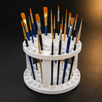 White two-tier folding brush holder filled with assorted artist brushes on a dark background