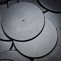 Cluster of 90mm round bases stacked on a black surface, close-up detail.
