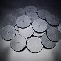 A group of 90mm round bases in a pile on a black background.