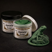 Aves Apoxie Sculpt 1lb Green — Part A tub open showing green putty, Part B tub behind, with a detailed sculpted iguana figure demonstrating the material's fine detail capability