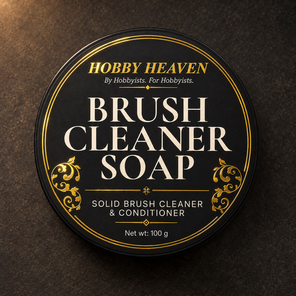 Top view of the black tin lid, gold-foil label: Brush Cleaner Soap, solid brush cleaner and conditioner, 100 g