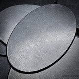 Matte black 105x70mm oval plain plastic wargaming bases with a fine textured top, injection-moulded ABS, shown in a pile.
