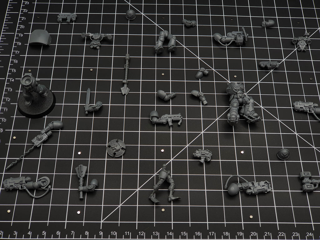 Wargaming miniature arms, weapons and torso parts laid out on a cutting mat with tiny disc magnets for weapon swaps