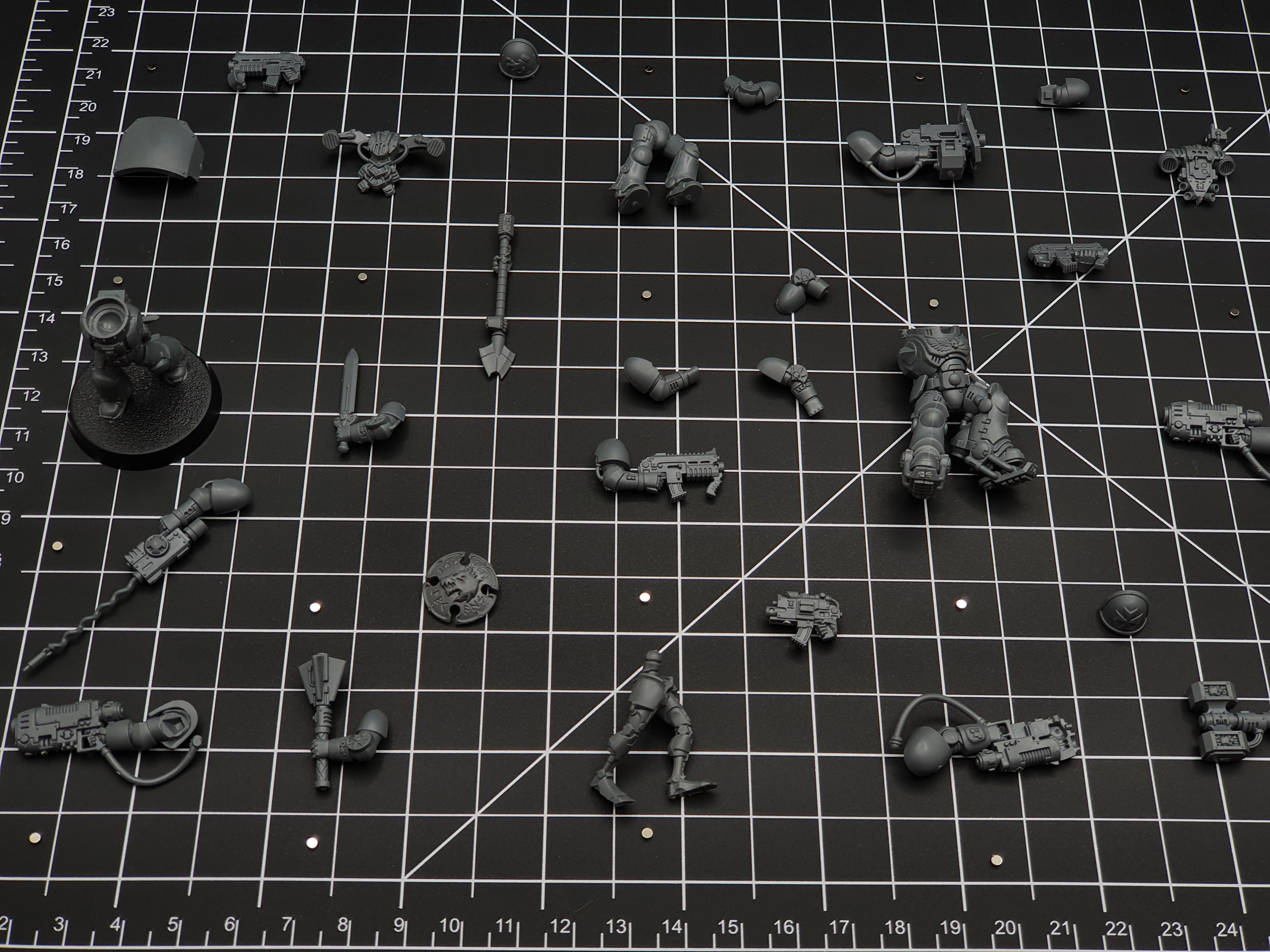 Wargaming miniature arms, weapons and torso parts laid out on a cutting mat with tiny disc magnets for weapon swaps