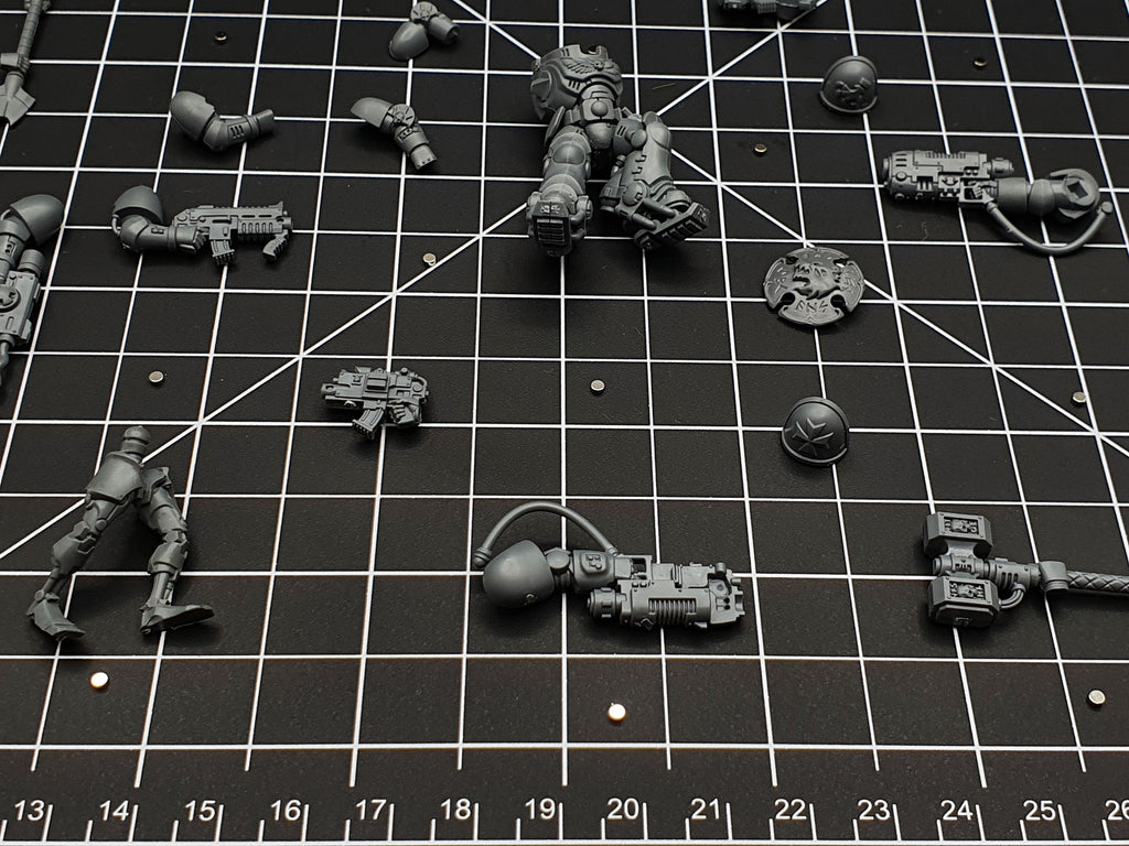 Close-up of magnetised miniature parts on a cutting mat, small disc magnets fitted for arm and weapon swaps