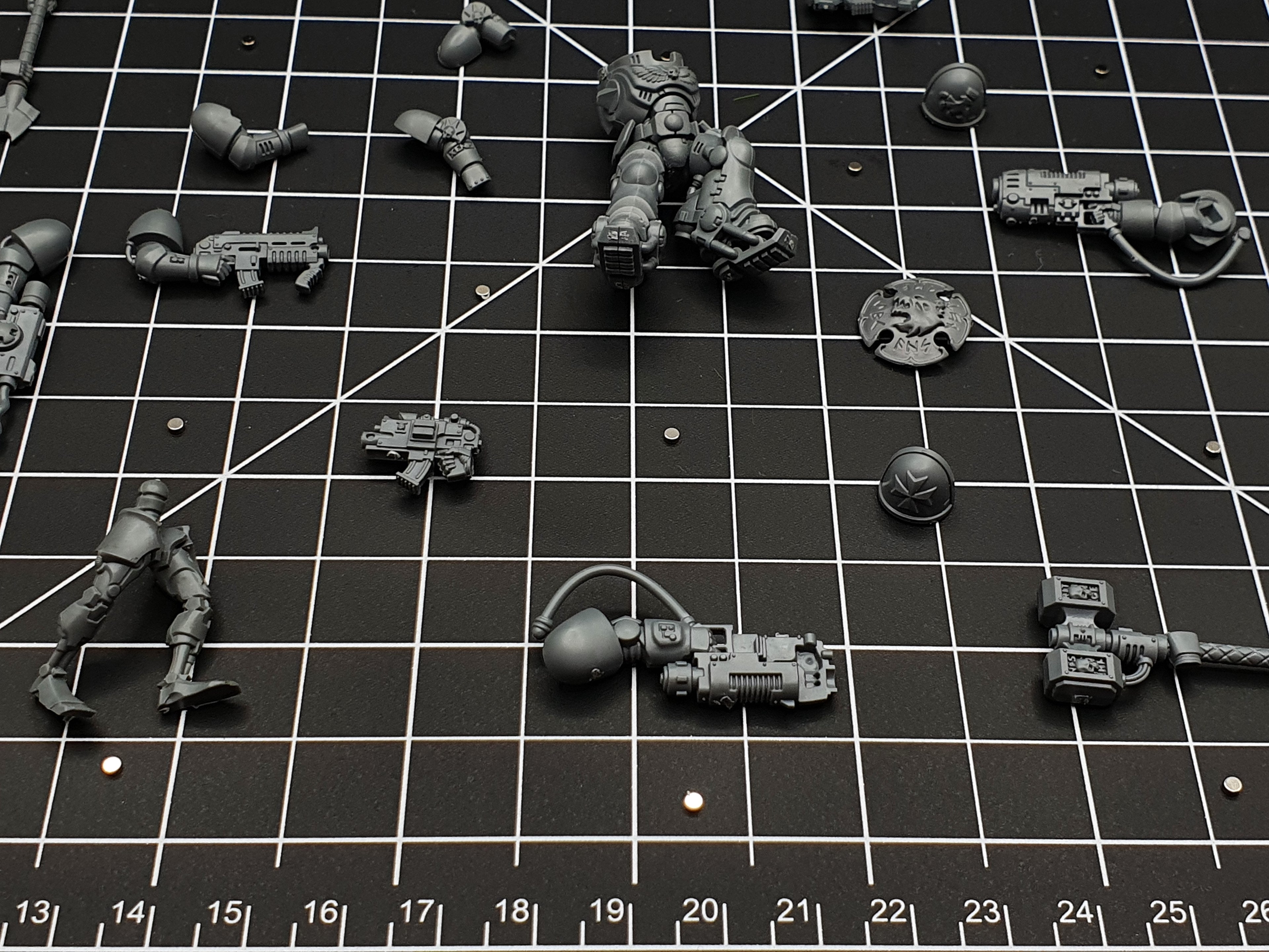 Close-up of magnetised miniature parts on a cutting mat, small disc magnets fitted for arm and weapon swaps