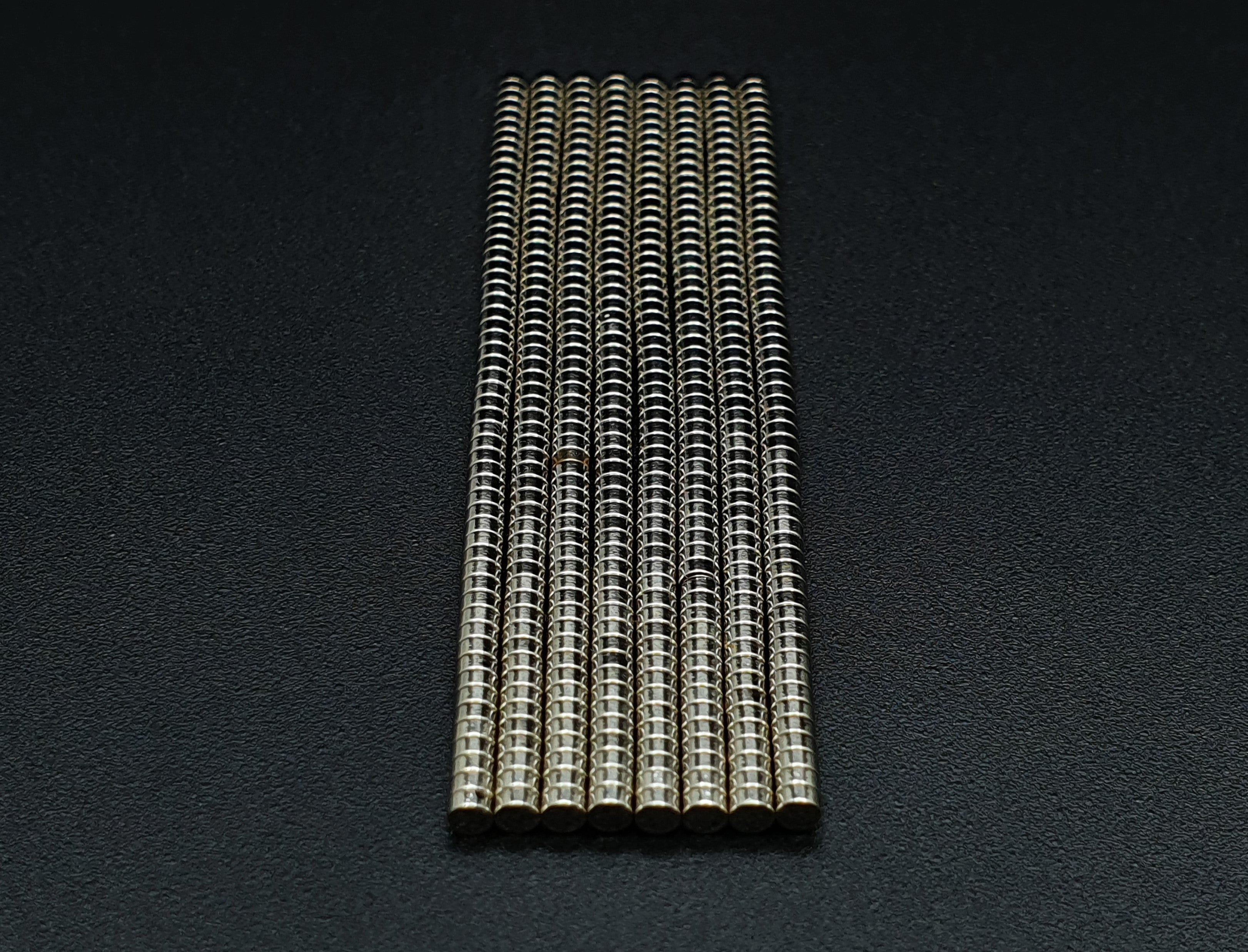 Stacked columns of 2 x 1 mm neodymium disc magnets standing upright on a dark background
