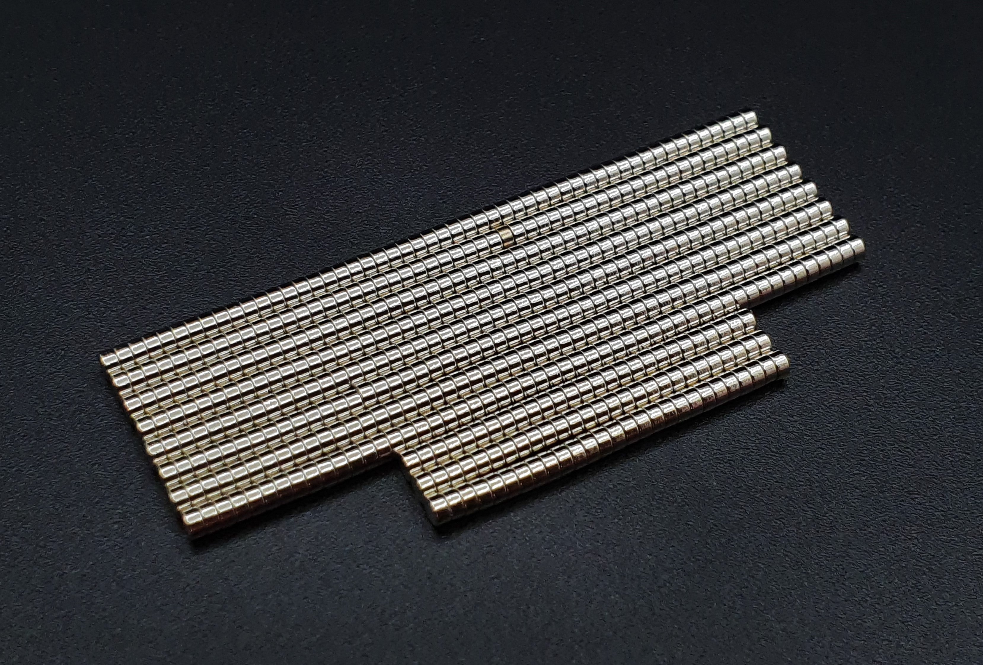 Two overlapping groups of stacked 2 x 1 mm neodymium disc magnets on a dark background