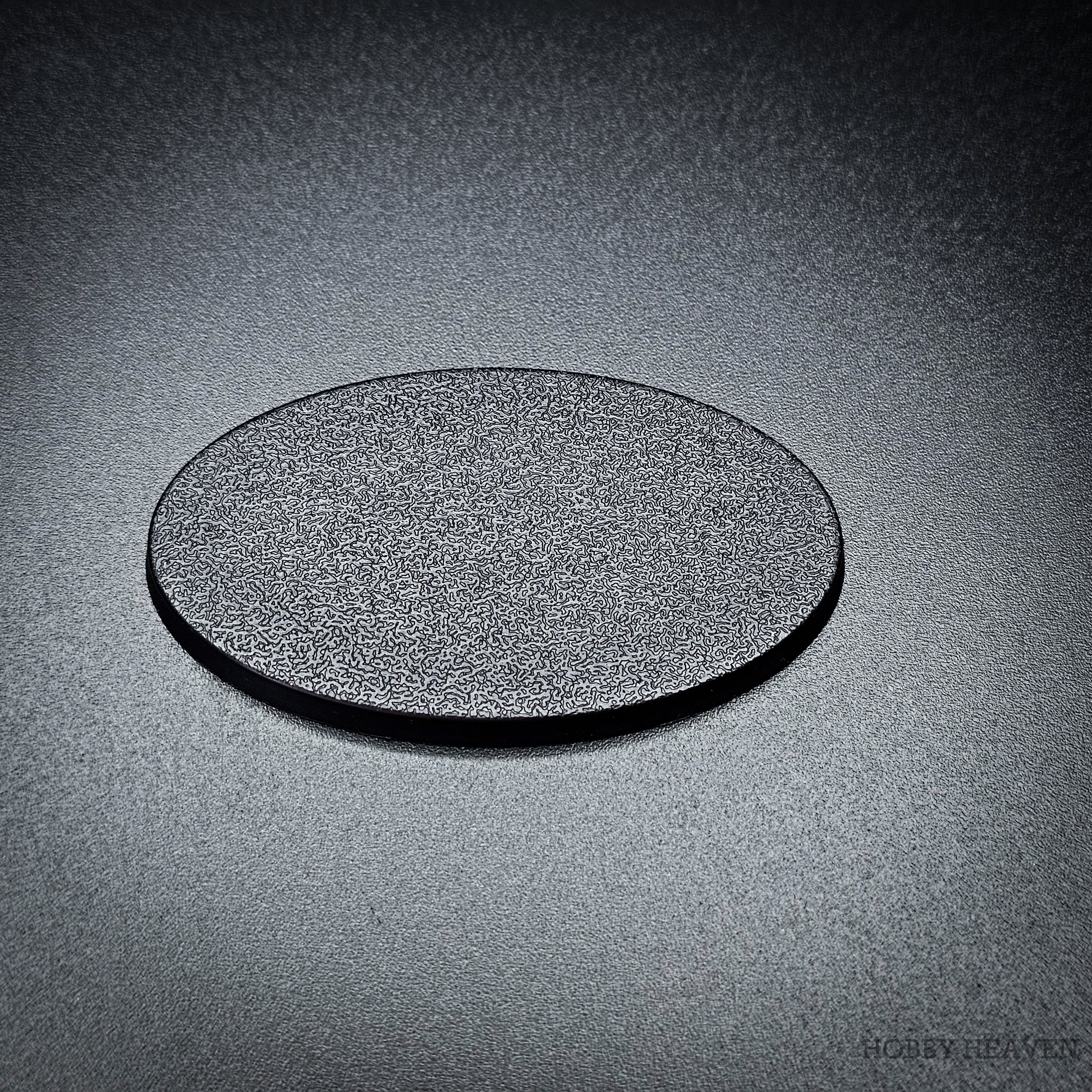 Single 60x35mm oval plain plastic base in matte black, angled to show its fine textured top face