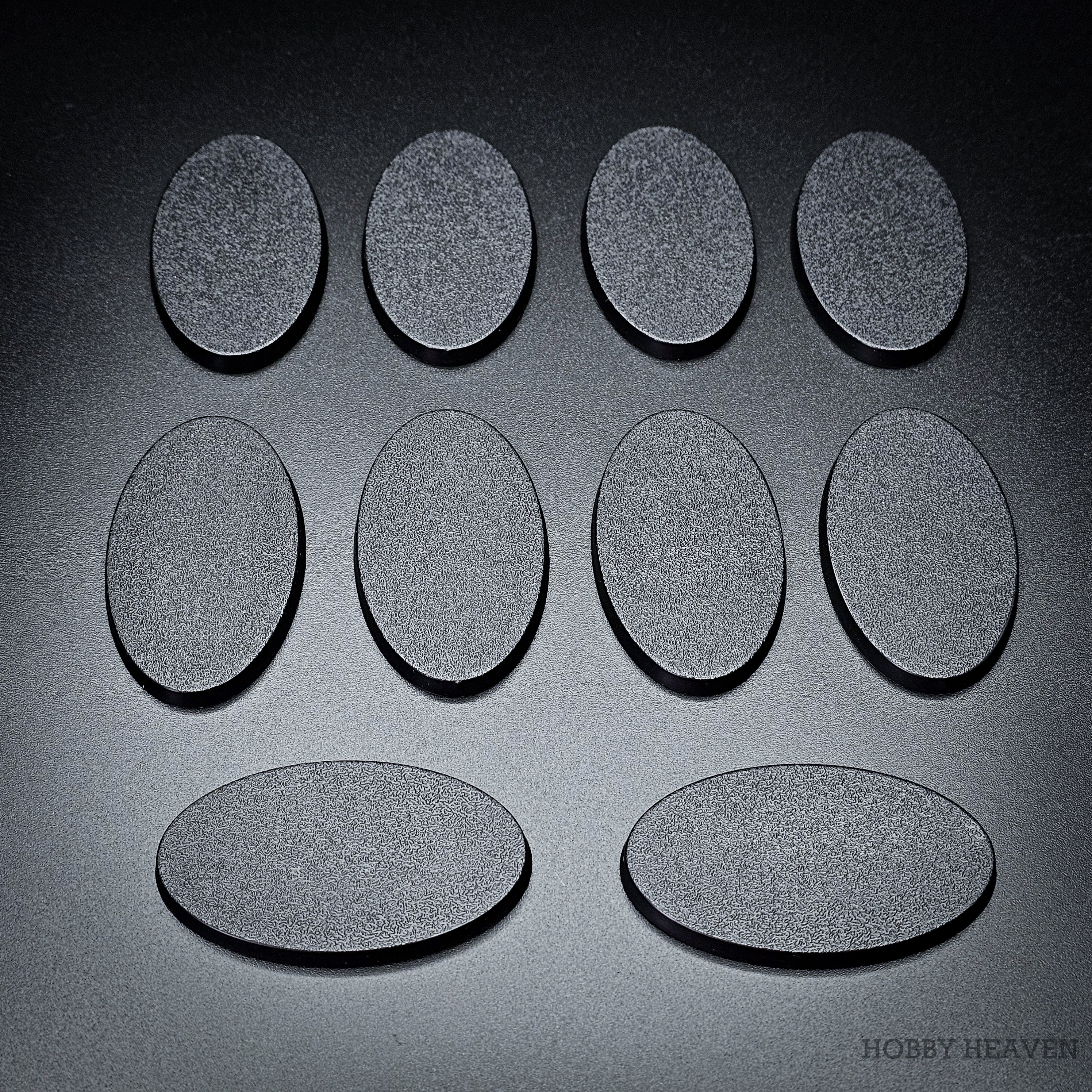 Ten 60x35mm oval plain plastic bases laid out in rows, each showing its matte black textured top