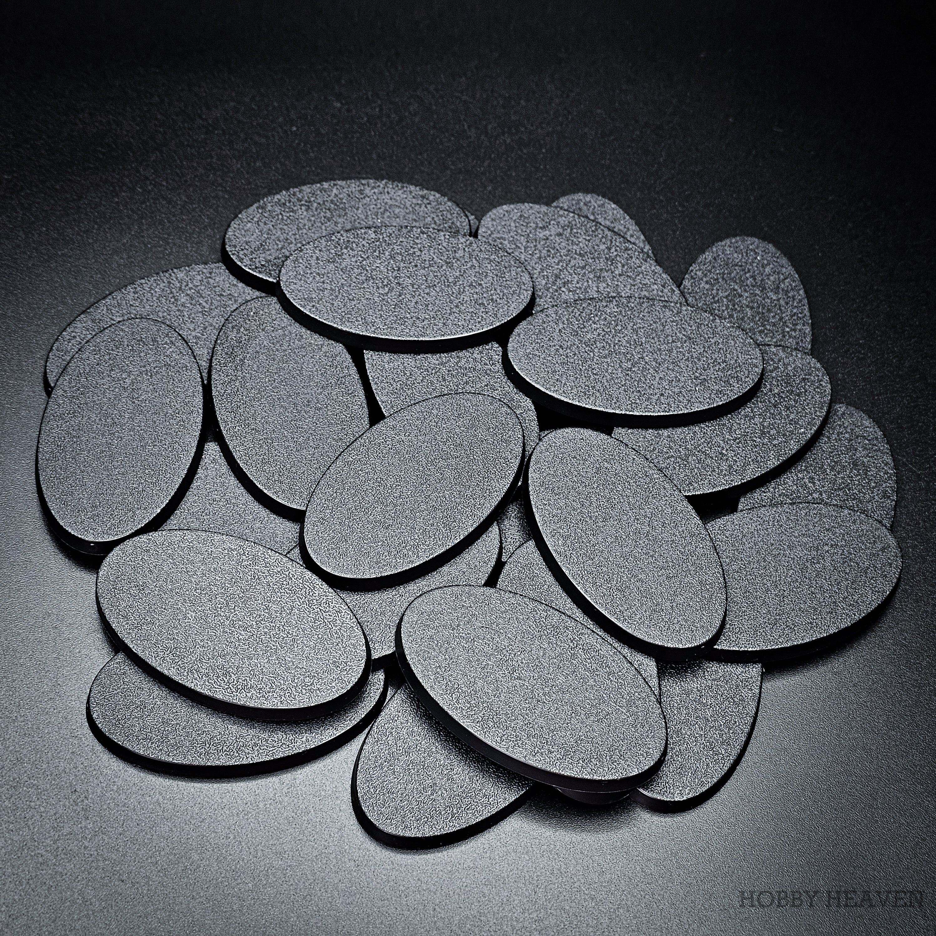 A pile of 60x35mm oval plain plastic bases overlapping, textured tops up, on a grey backdrop