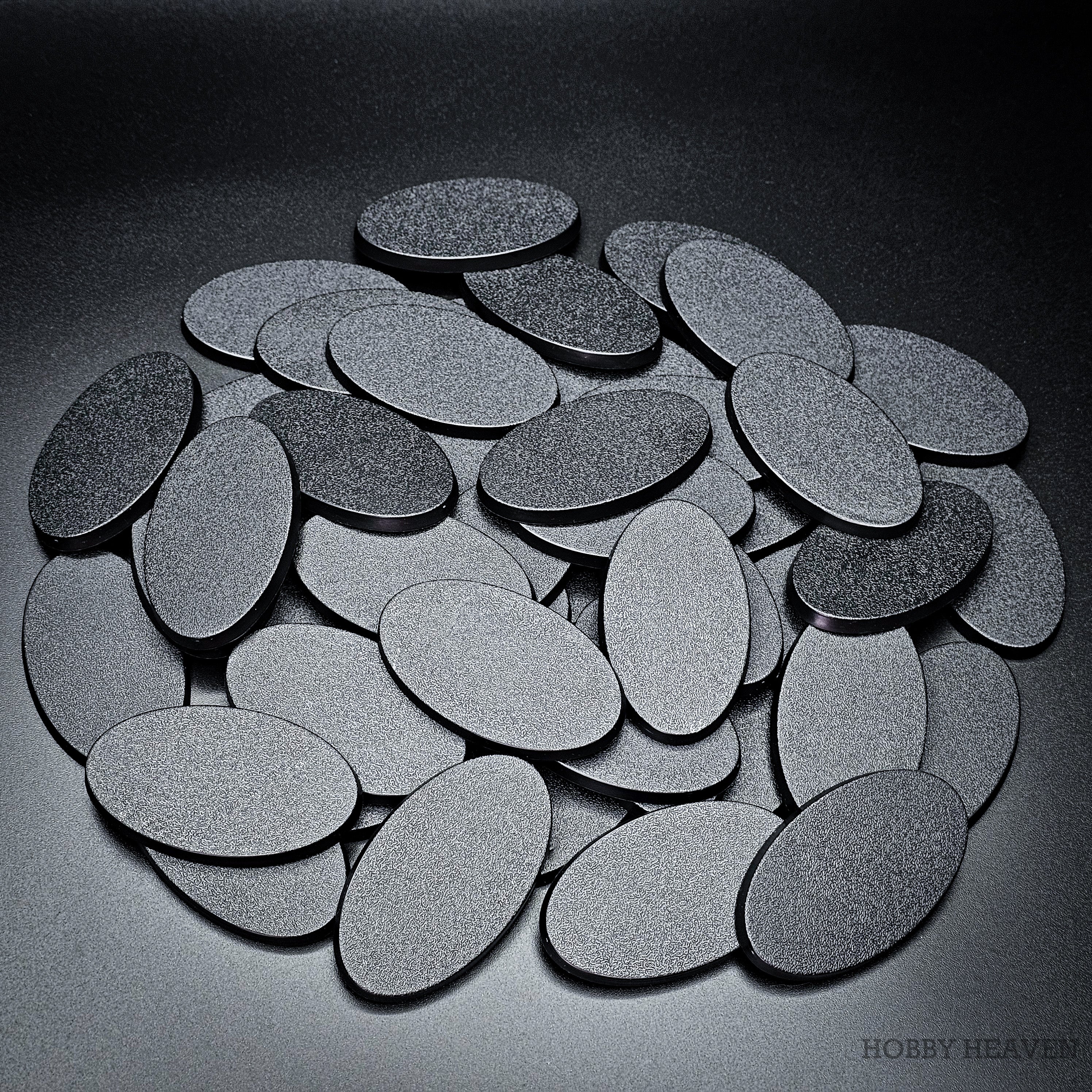 A deep heap of 60x35mm oval plain plastic bases stacked several layers thick, tops and edges visible