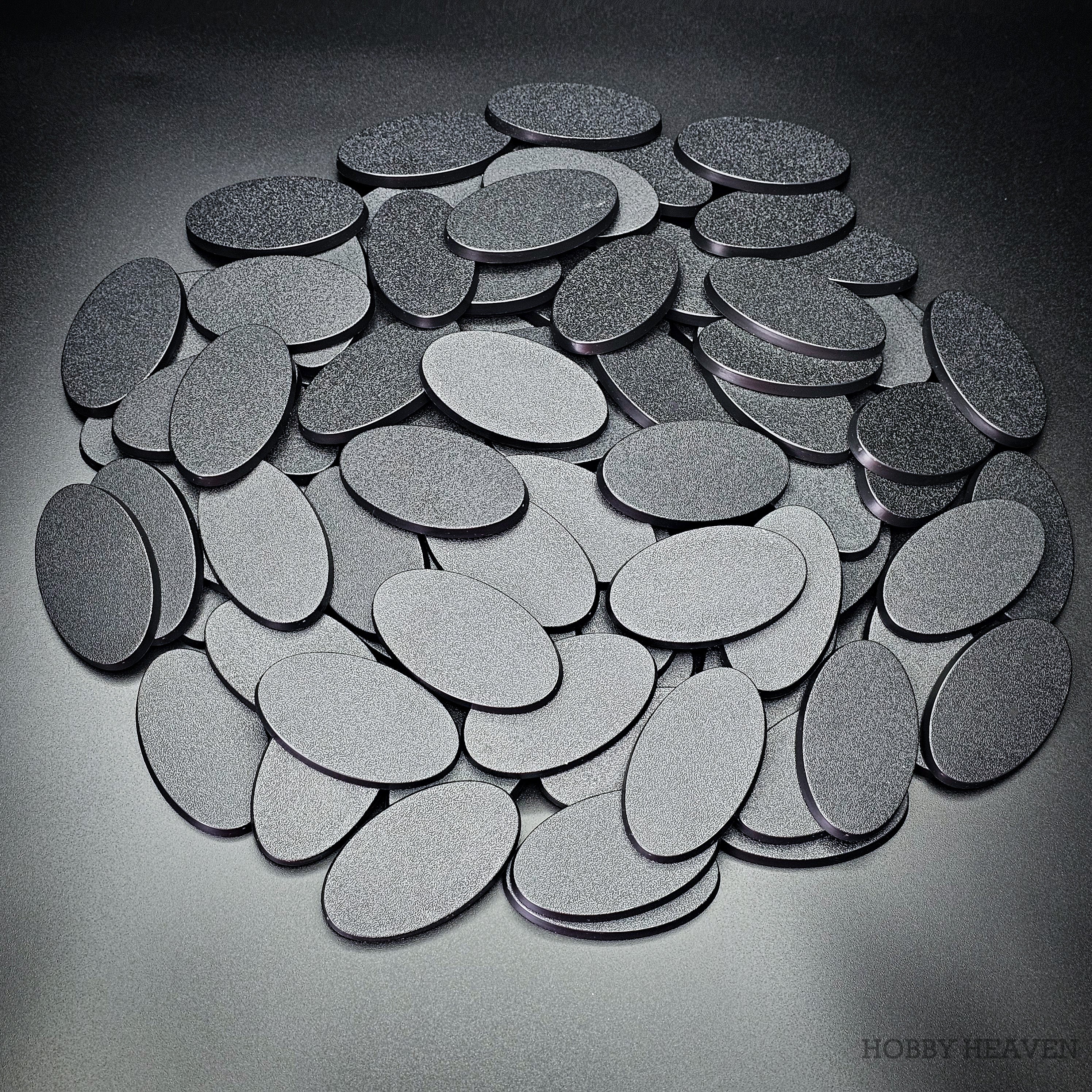 A bulk quantity of 60x35mm oval plain plastic bases heaped together, textured tops facing up