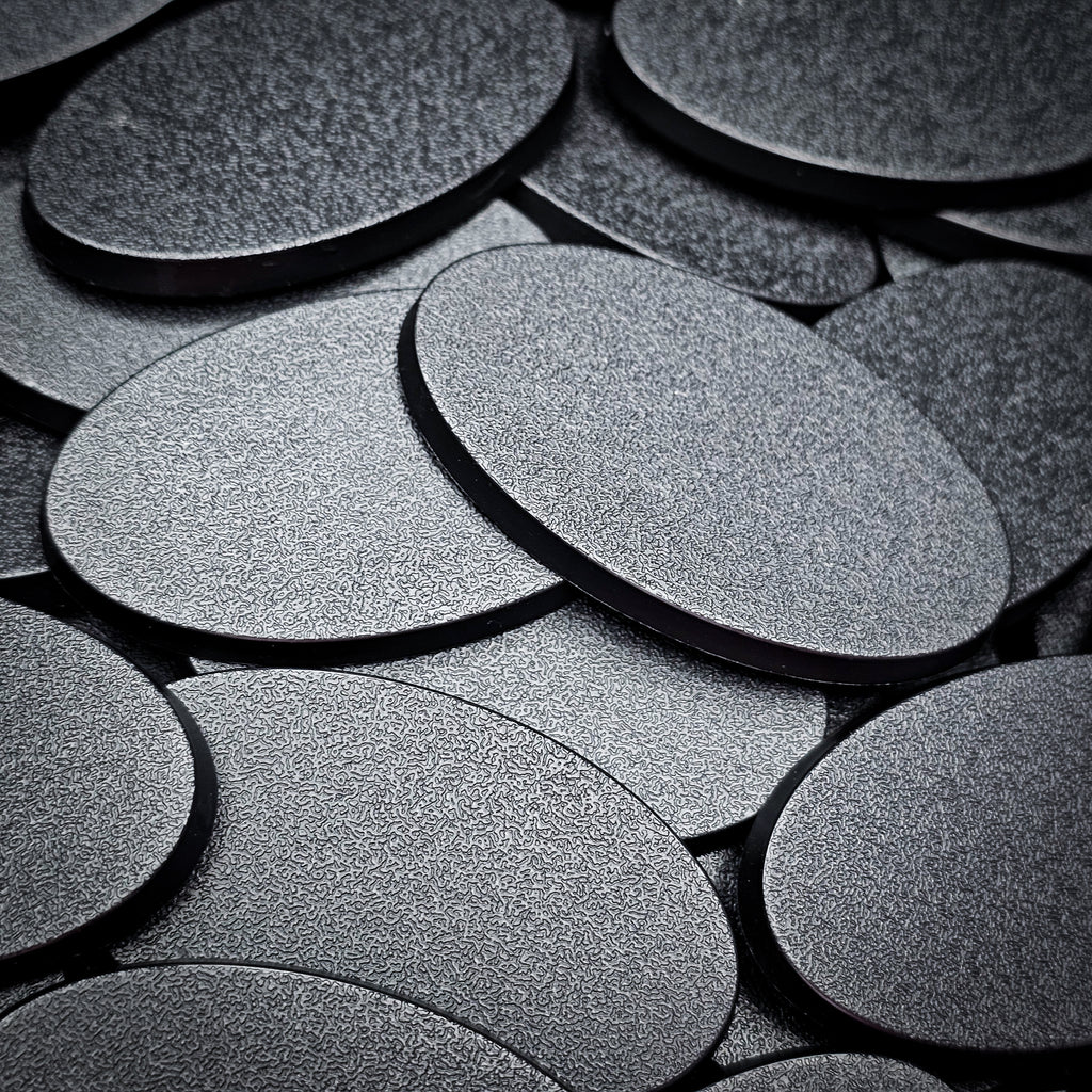 Overlapping 60x35mm oval plain plastic bases seen close up, their textured tops catching the light