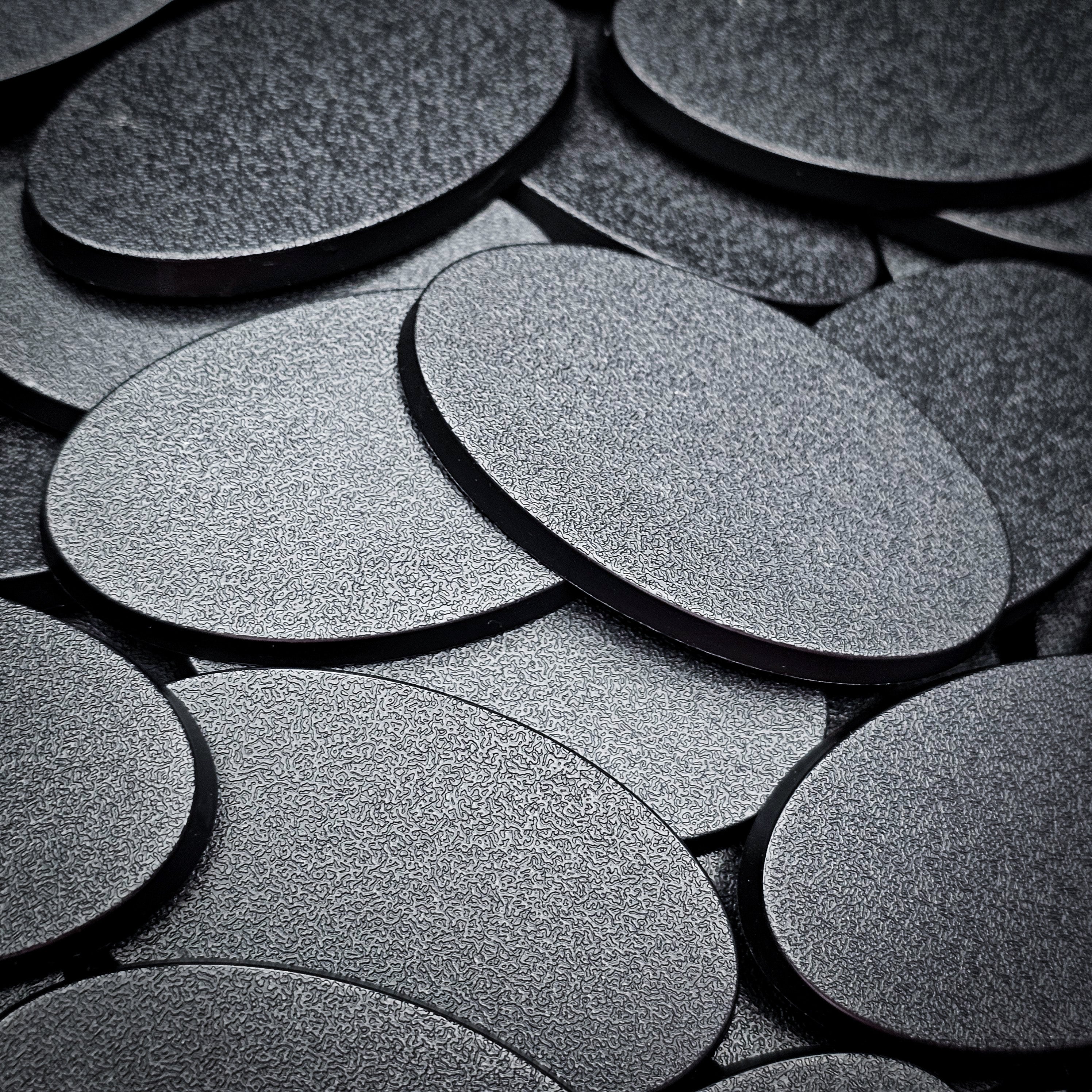 Overlapping 60x35mm oval plain plastic bases seen close up, their textured tops catching the light