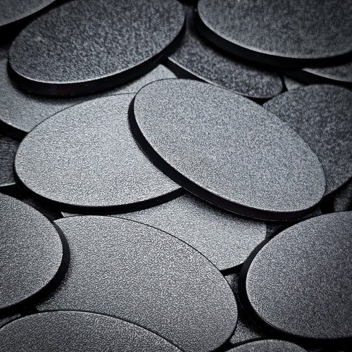 Overlapping 60x35mm oval plain plastic bases seen close up, their textured tops catching the light