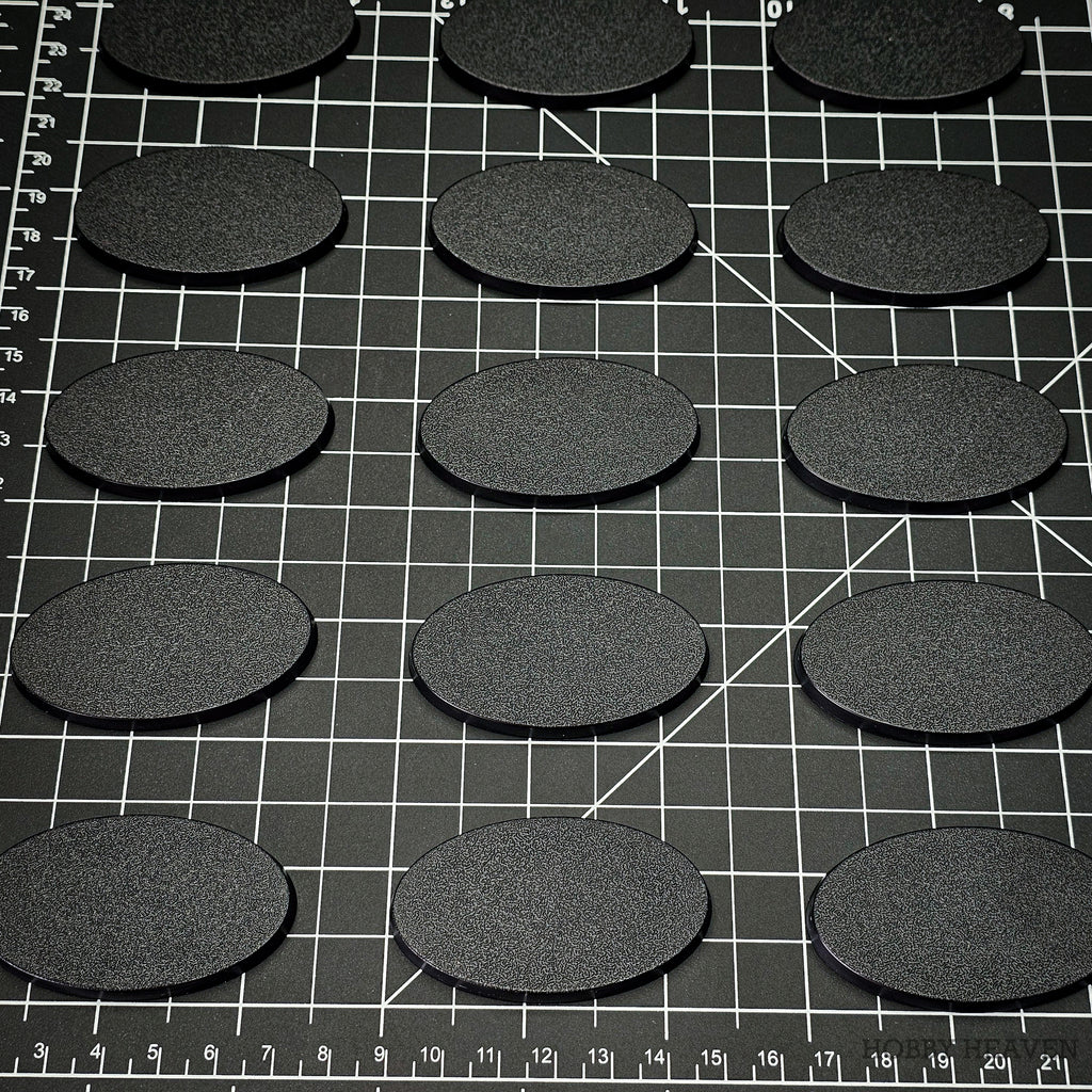 60x35mm oval plain plastic bases arranged on a gridded cutting mat alongside a centimetre scale