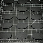 60x35mm oval plain plastic bases arranged on a gridded cutting mat alongside a centimetre scale