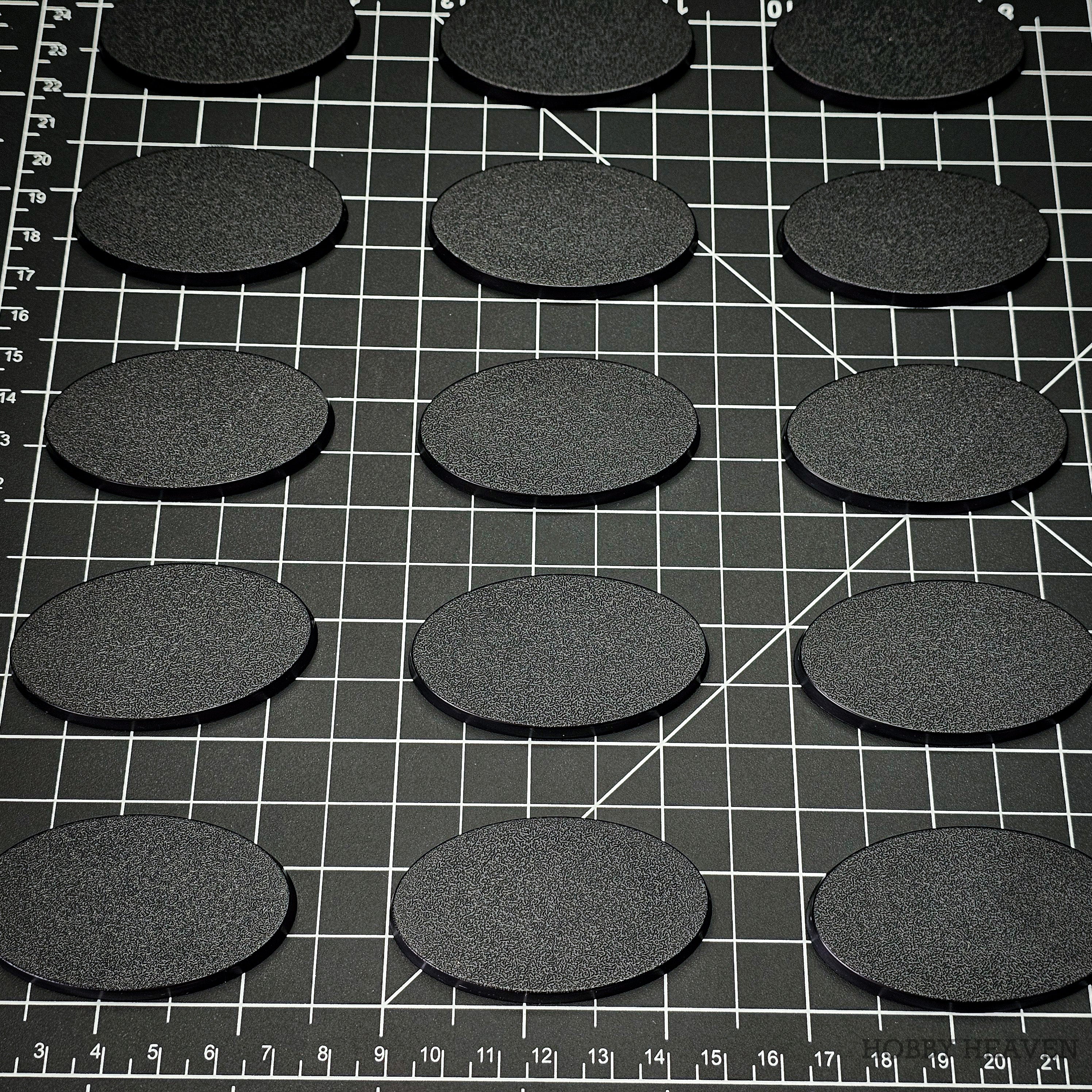 60x35mm oval plain plastic bases arranged on a gridded cutting mat alongside a centimetre scale