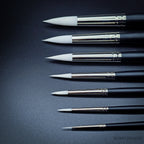 Close-up of nine Snowdrop brush heads in sizes 0 to 16 showing the tapered white taklon points and progressive size increase