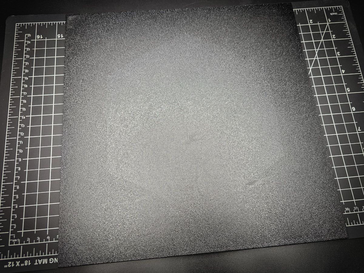 Angled photograph of the 300mm square textured PETG base on a cutting mat with ruler markings visible for scale.
