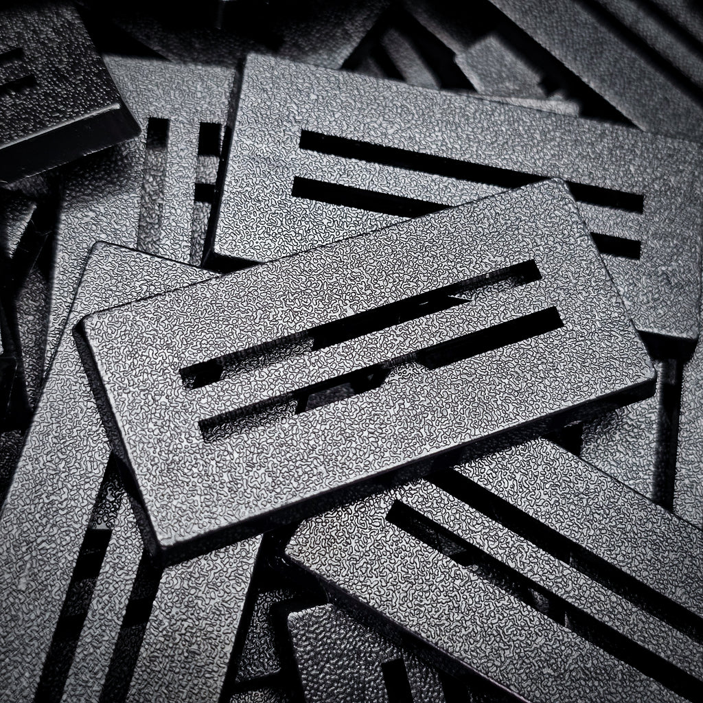 Angled close-up of a 50x25mm slotted base: bevelled edge, two parallel slots and textured top surface