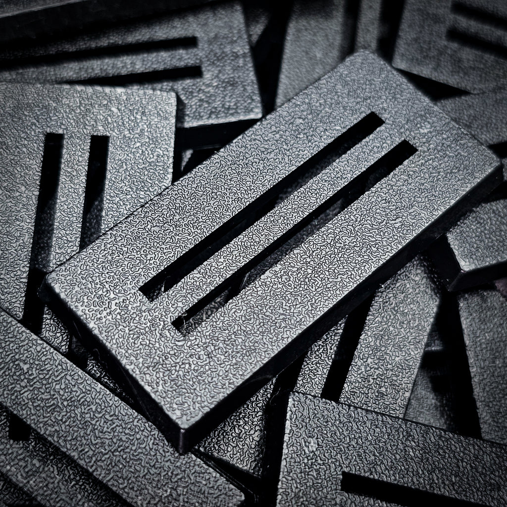 Close-up of black 50x25mm rectangle slotted bases showing the two parallel slots and fine textured top