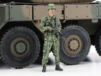 The full-body crew figure holding a rifle beside the wheels