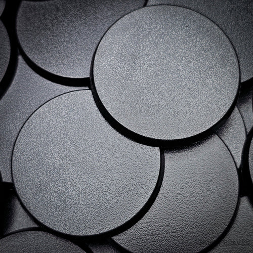 Black 50mm round plain plastic wargaming bases with a fine textured top, injection-moulded ABS, shown in a pile.