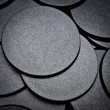 Black 60mm round plain plastic wargaming bases with a fine textured top, injection-moulded ABS, shown in a pile.