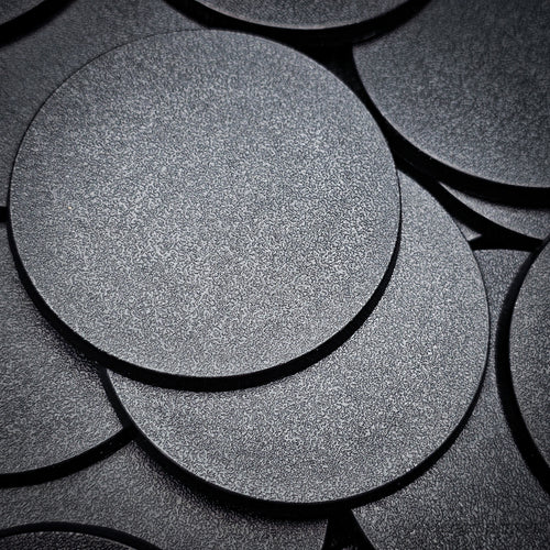 Black 60mm round plain plastic wargaming bases with a fine textured top, injection-moulded ABS, shown in a pile.