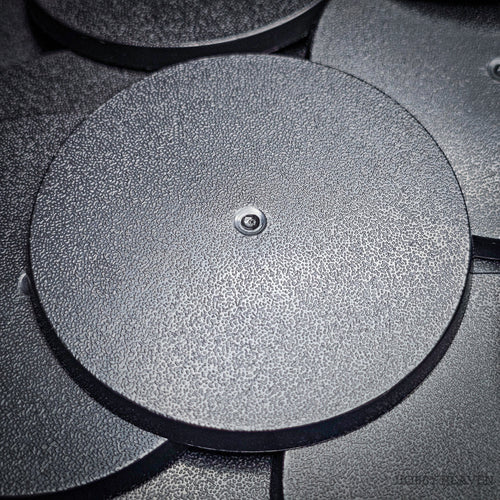 Black 70mm round plain plastic wargaming bases with a fine textured top, injection-moulded ABS, shown in a pile.