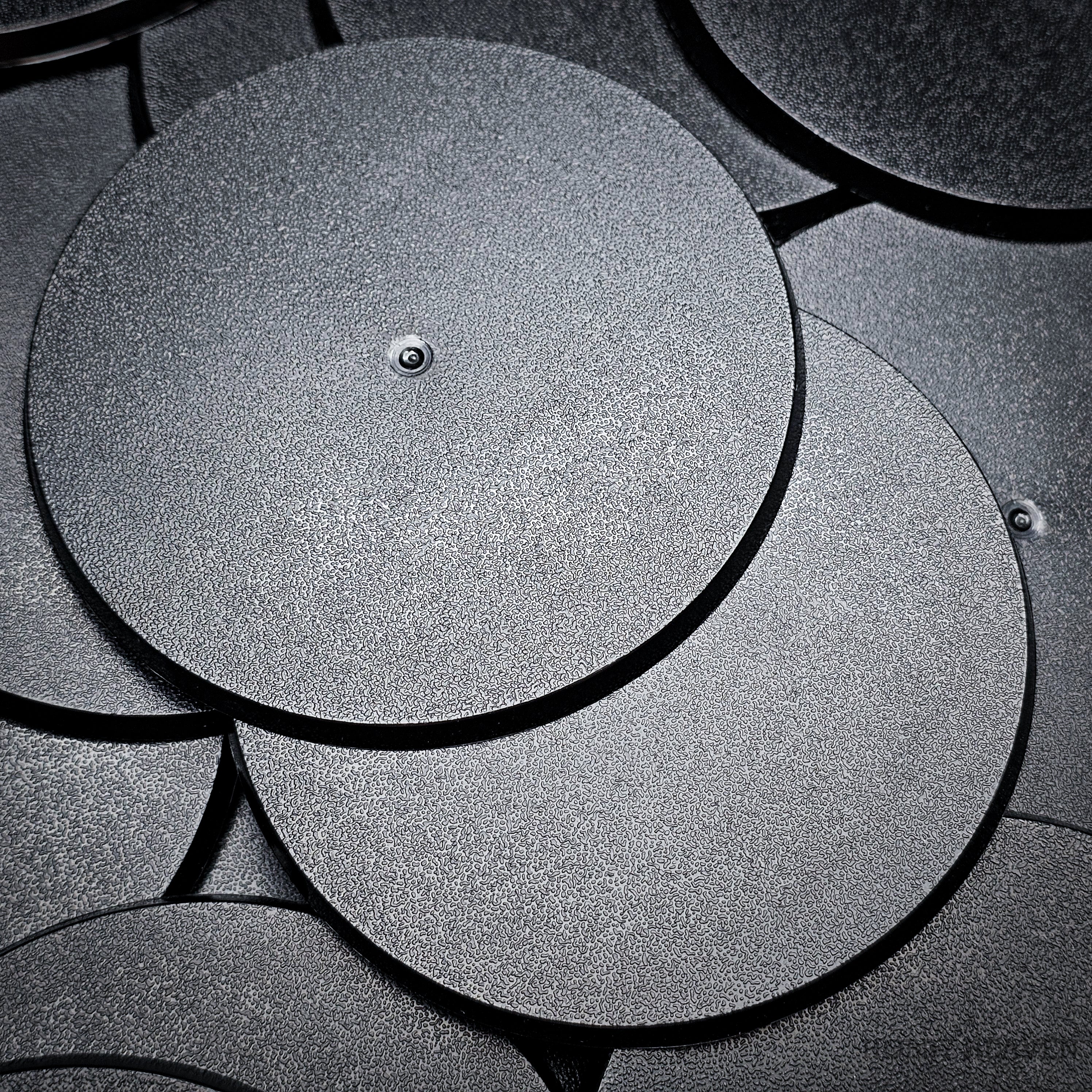 Cluster of 90mm round bases stacked on a black surface, close-up detail.