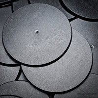 Cluster of 90mm round bases stacked on a black surface, close-up detail.
