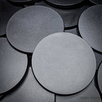 Close-up of clustered 100mm round bases on a dark surface.
