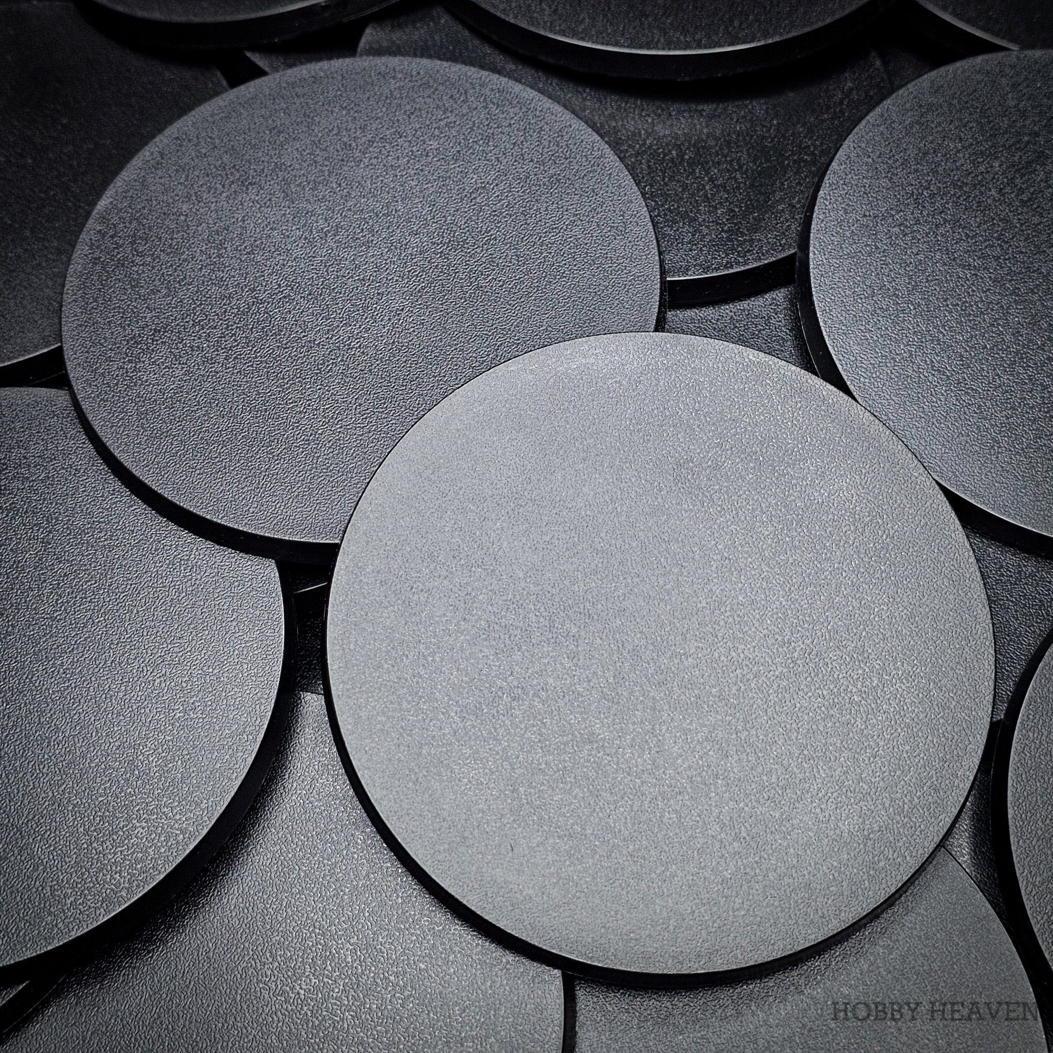 Close-up of clustered 100mm round bases on a dark surface.