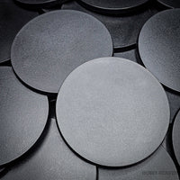 Close-up of clustered 100mm round bases on a dark surface.
