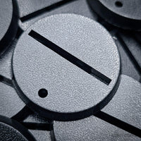 lose-up of 32mm round slotted bases lying on a pile of other bases.
