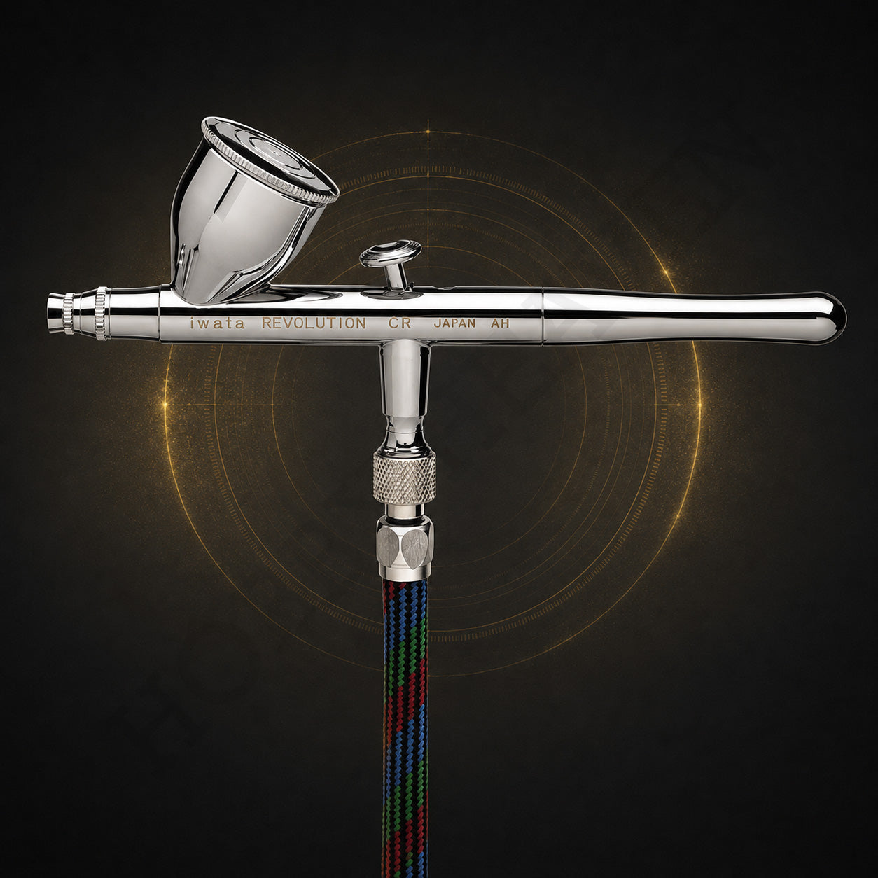 Iwata Revolution CR seen from the front, connected to a braided multicoloured airbrush hose
