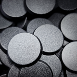 Black 25mm round plain plastic wargaming bases with a fine textured top, injection-moulded ABS, shown in a pile.