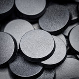 Black 32mm round plain plastic wargaming bases with a fine textured top, injection-moulded ABS, shown in a pile.