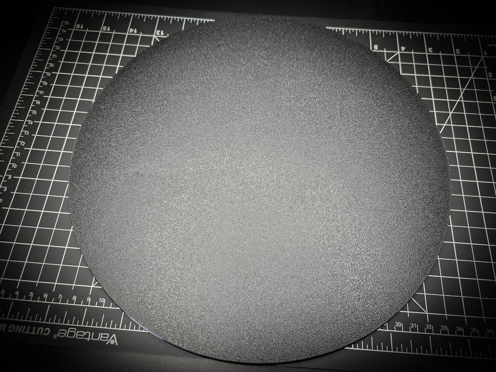 Angled photograph of the 300mm round textured PETG base on a cutting mat, showing the thin 6mm profile and textured surface.