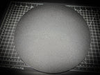 Angled photograph of the 300mm round textured PETG base on a cutting mat, showing the thin 6mm profile and textured surface.