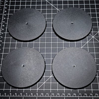 Four 90mm round bases arranged on a black cutting mat.
