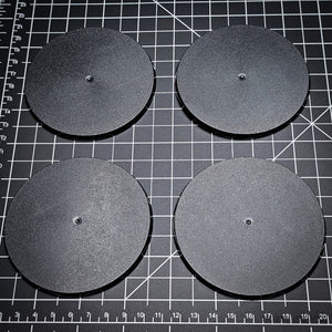 Four 90mm round bases arranged on a black cutting mat.