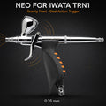 Neo for Iwata TRN1 trigger airbrush against black, 7 ml gravity cup above an orange-ribbed pistol grip