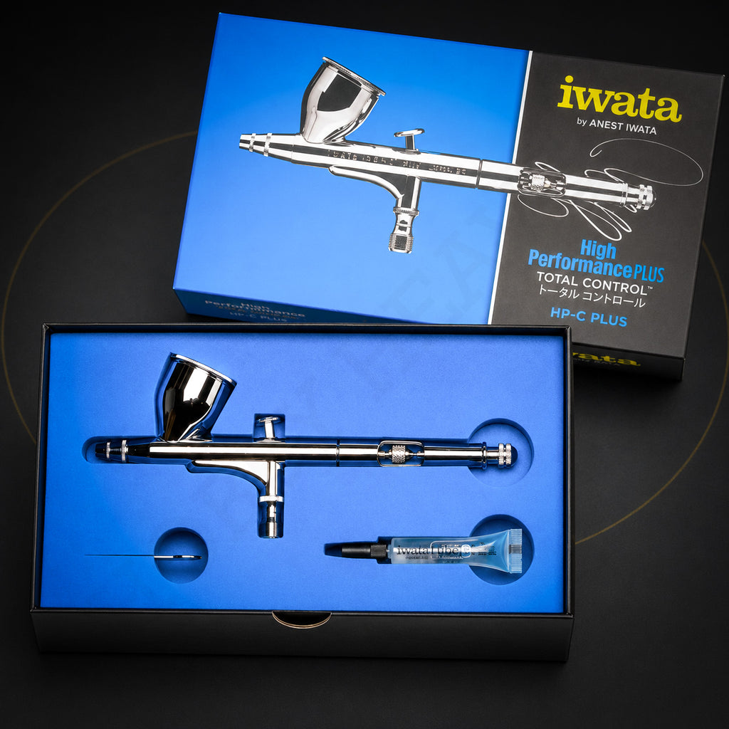 Iwata HP-C Plus in its open blue High Performance Plus box with a tube of Iwata Lube and a slim metal part