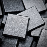 Matte black 20mm square plain plastic wargaming bases with a fine textured top, injection-moulded ABS, shown in a pile.