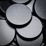 Black 28mm round plain plastic wargaming bases with a fine textured top, injection-moulded ABS, shown in a pile.