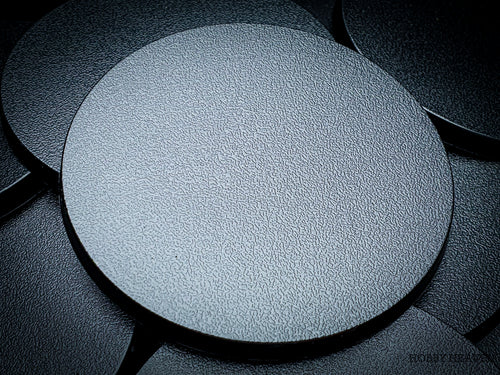 Black 80mm round plain plastic wargaming bases with a fine textured top, injection-moulded ABS, shown in a pile.